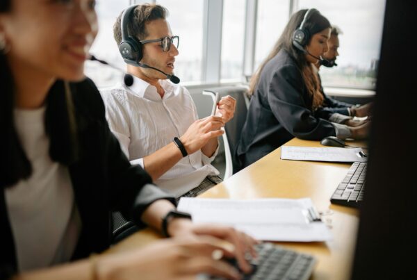 people sitting at a desk in an office, wearing headsets typing on their keyboards